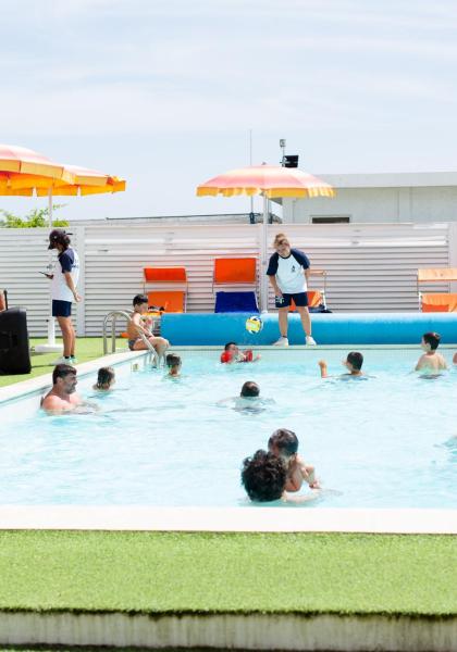 Überfülltes Schwimmbad mit Kindern und orangefarbenen Sonnenschirmen.