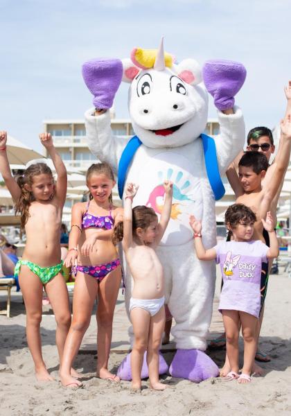 Kinder mit Einhorn-Maskottchen am Strand, lächelnd und glücklich.