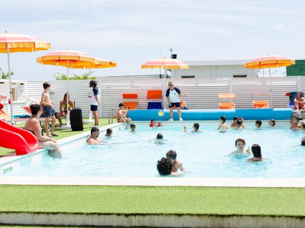Piscina all'aperto con bambini e ombrelloni colorati.