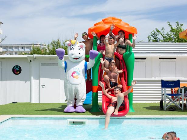Bambini giocano in piscina con una mascotte colorata.