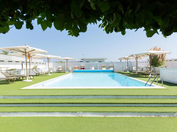 Outdoor pool with sunbeds and umbrellas, surrounded by artificial grass.