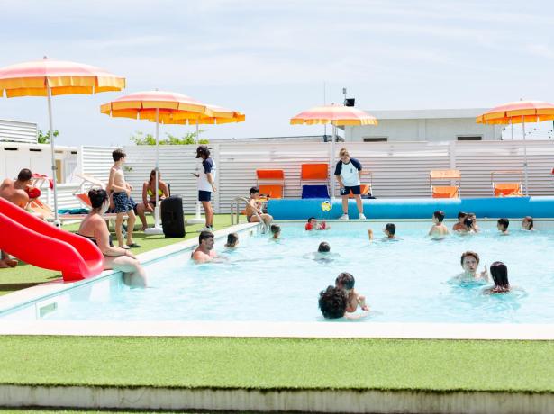 Piscina affollata con bambini e ombrelloni arancioni.