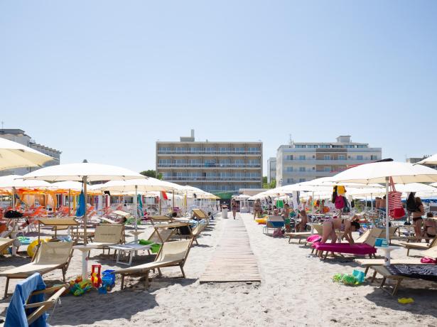 Spiaggia affollata con ombrelloni e lettini, edifici sullo sfondo.