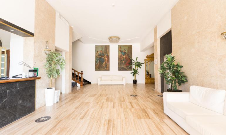 Elegante hall con divani bianchi, piante e dipinti.