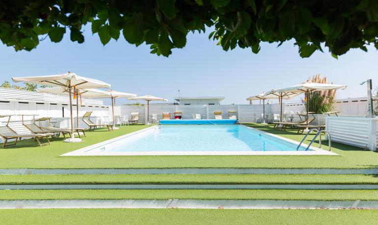Piscine extérieure avec transats et parasols, entourée de gazon artificiel.