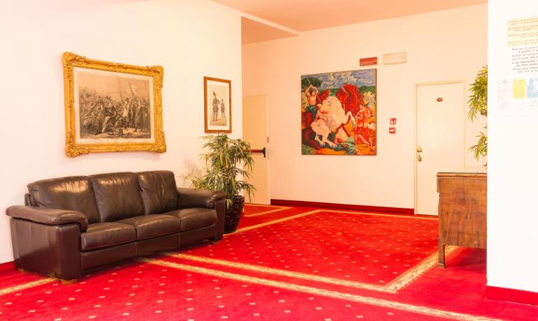 Sala d'attesa con divano in pelle, tappeto rosso e opere d'arte alle pareti.