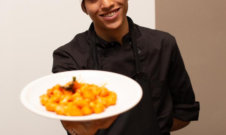 Koch präsentiert Tomaten-Gnocchi mit einem Lächeln.