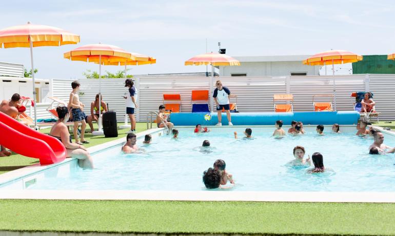 Crowded pool with children and orange umbrellas.