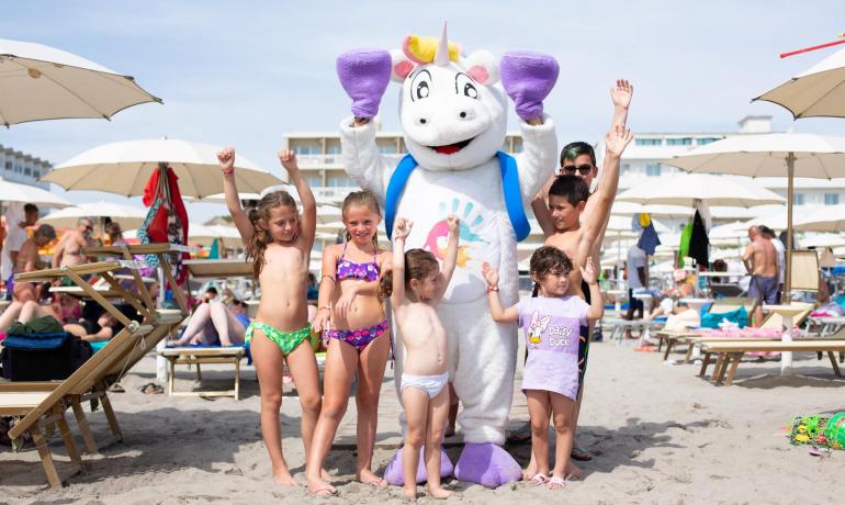 Children with unicorn mascot on the beach, smiling and happy.