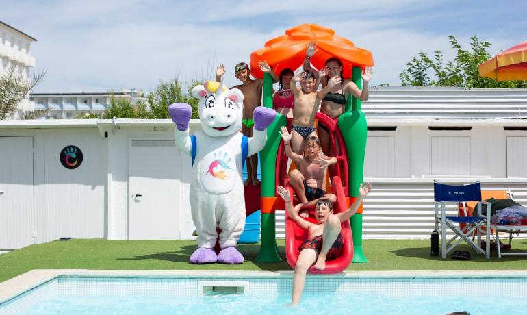 Kinder auf der Rutsche am Pool mit einem Einhorn-Maskottchen.