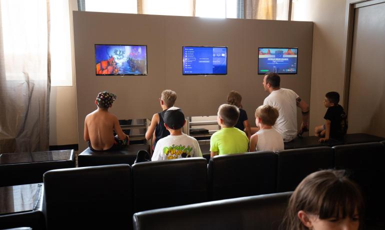 Kinder spielen Videospiele auf Bildschirmen in einem Spielzimmer.