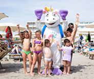 Persone festeggiano in spiaggia lanciando polvere colorata, creando un'atmosfera vivace e gioiosa.
