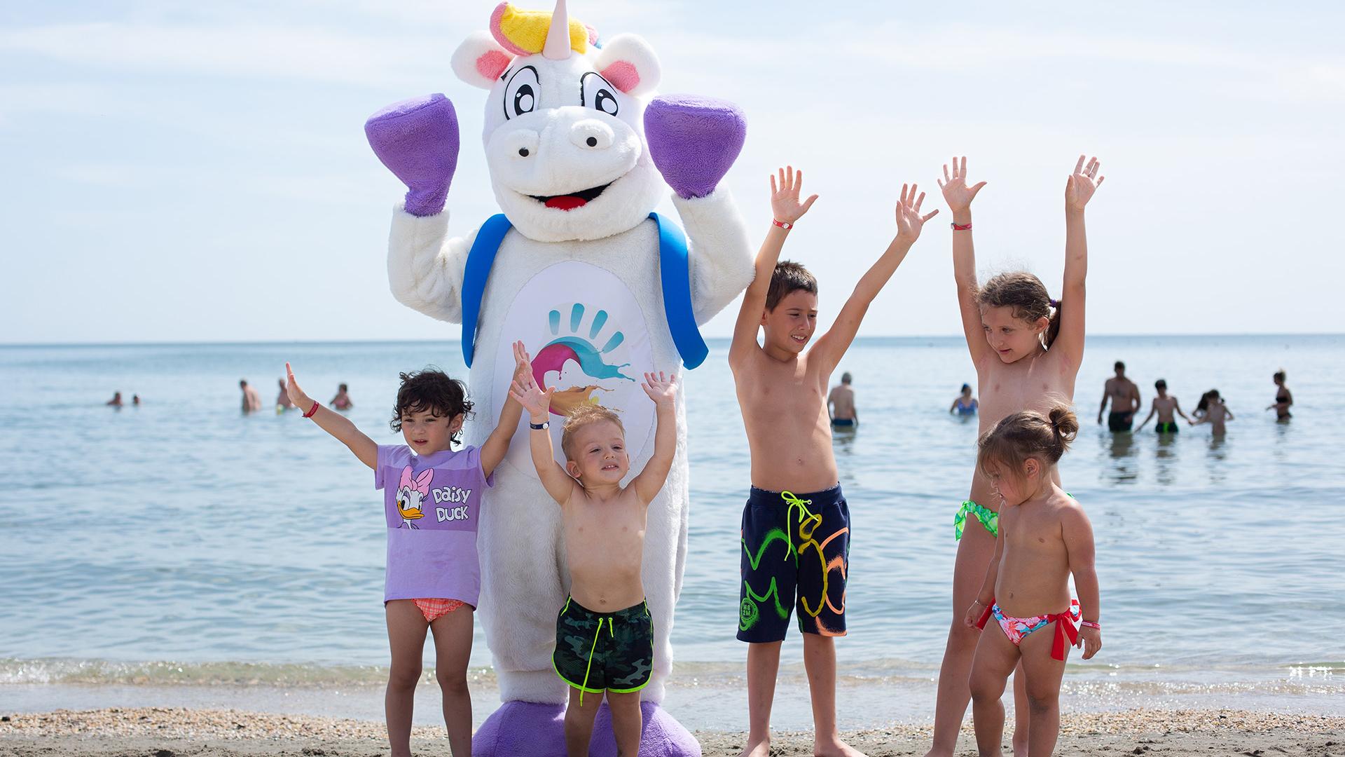 Bambino con braccioli arancioni vicino a piscina, ombrelloni colorati sullo sfondo.