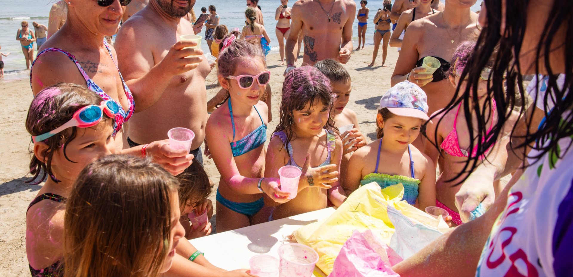 Bambini e adulti sorridenti sulla spiaggia, con colori vivaci e sole splendente.