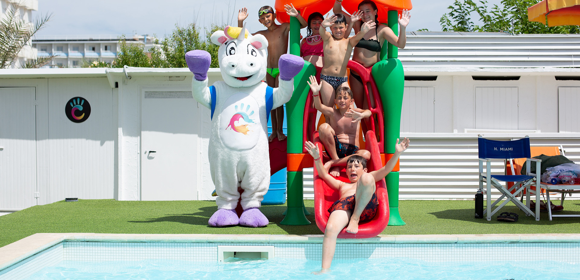 Bambina sorridente in piscina, si aggrappa al bordo sotto il sole estivo.