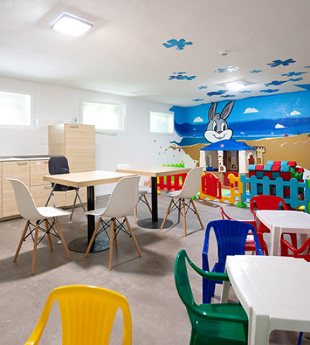 Area giochi per bambini con scivolo giallo e sedie colorate.