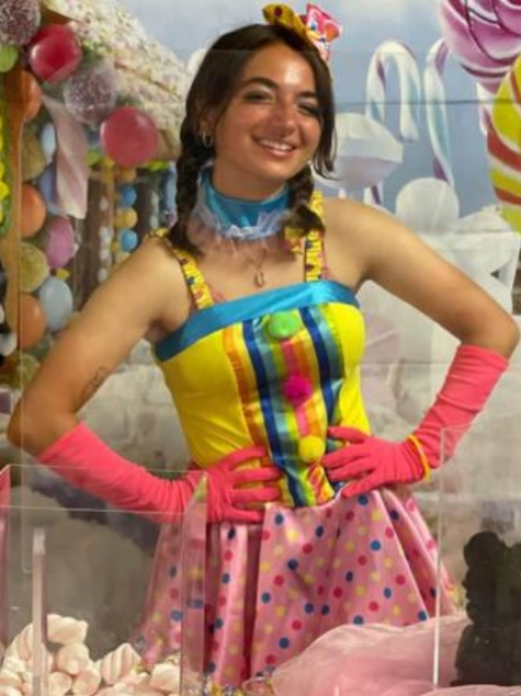 Ragazza in costume colorato da clown con sfondo di dolci e palloncini.