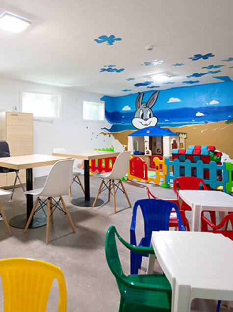 Area giochi per bambini con scivolo giallo e sedie colorate.