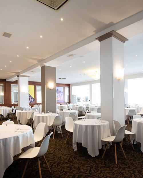 Elegantes Restaurant mit runden Tischen, weißen Stühlen und sanfter Beleuchtung.