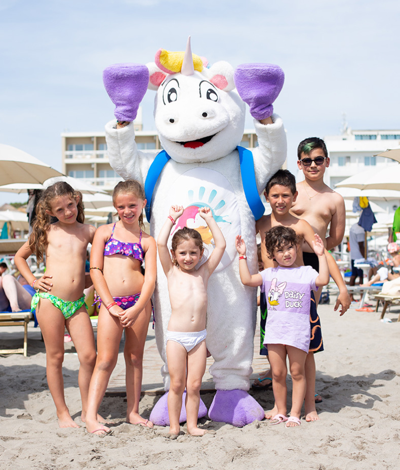 Ragazzo sistema ombrellone su spiaggia deserta, indossando occhiali da sole e maglietta blu.